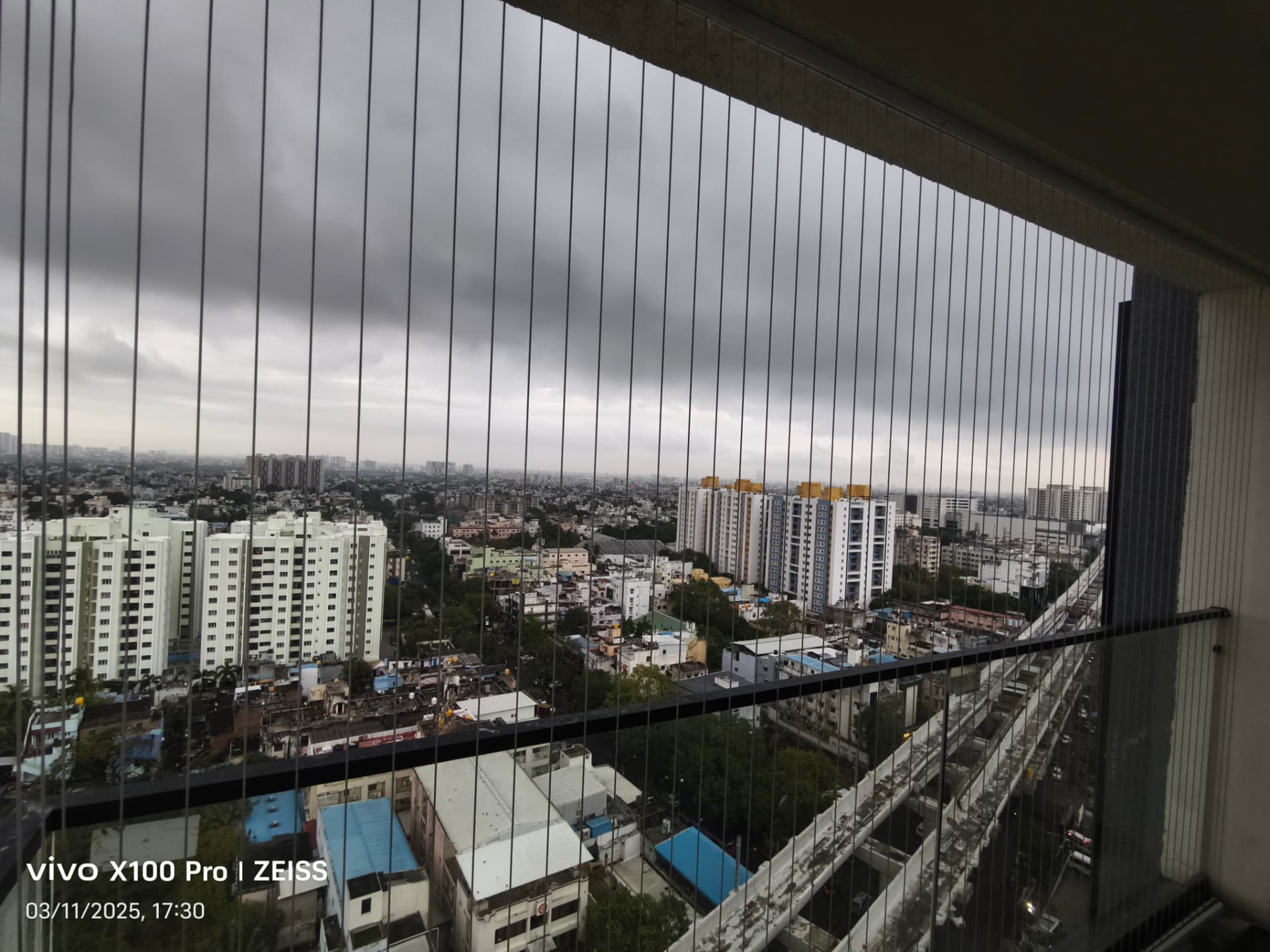 Wide balcony opening fitted with vertical stainless steel invisible grill cables, overlooking the Chennai city skyline.