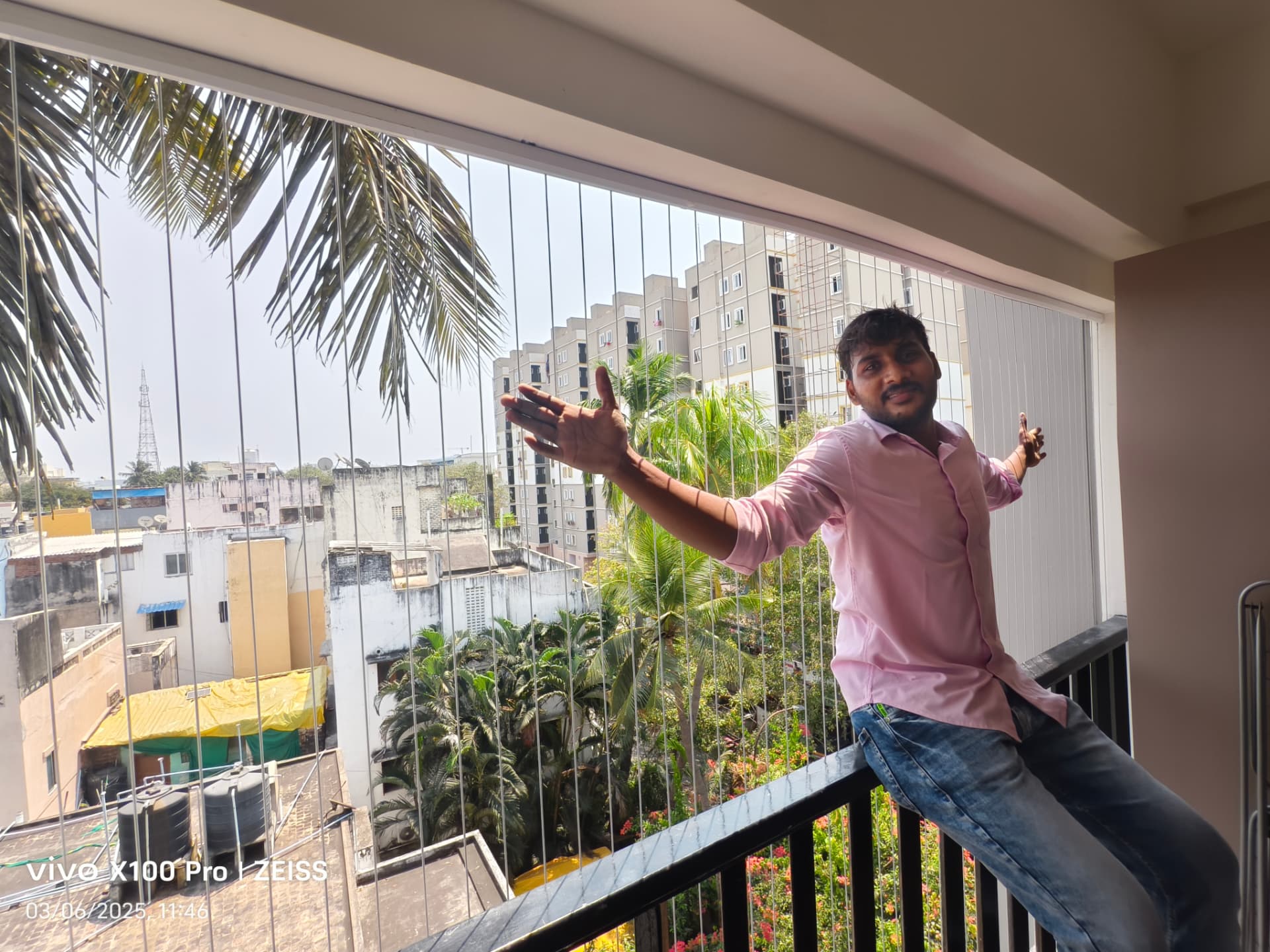 YPL installer showing newly fitted vertical invisible grill cables on an apartment balcony overlooking palm trees and towers in Chennai