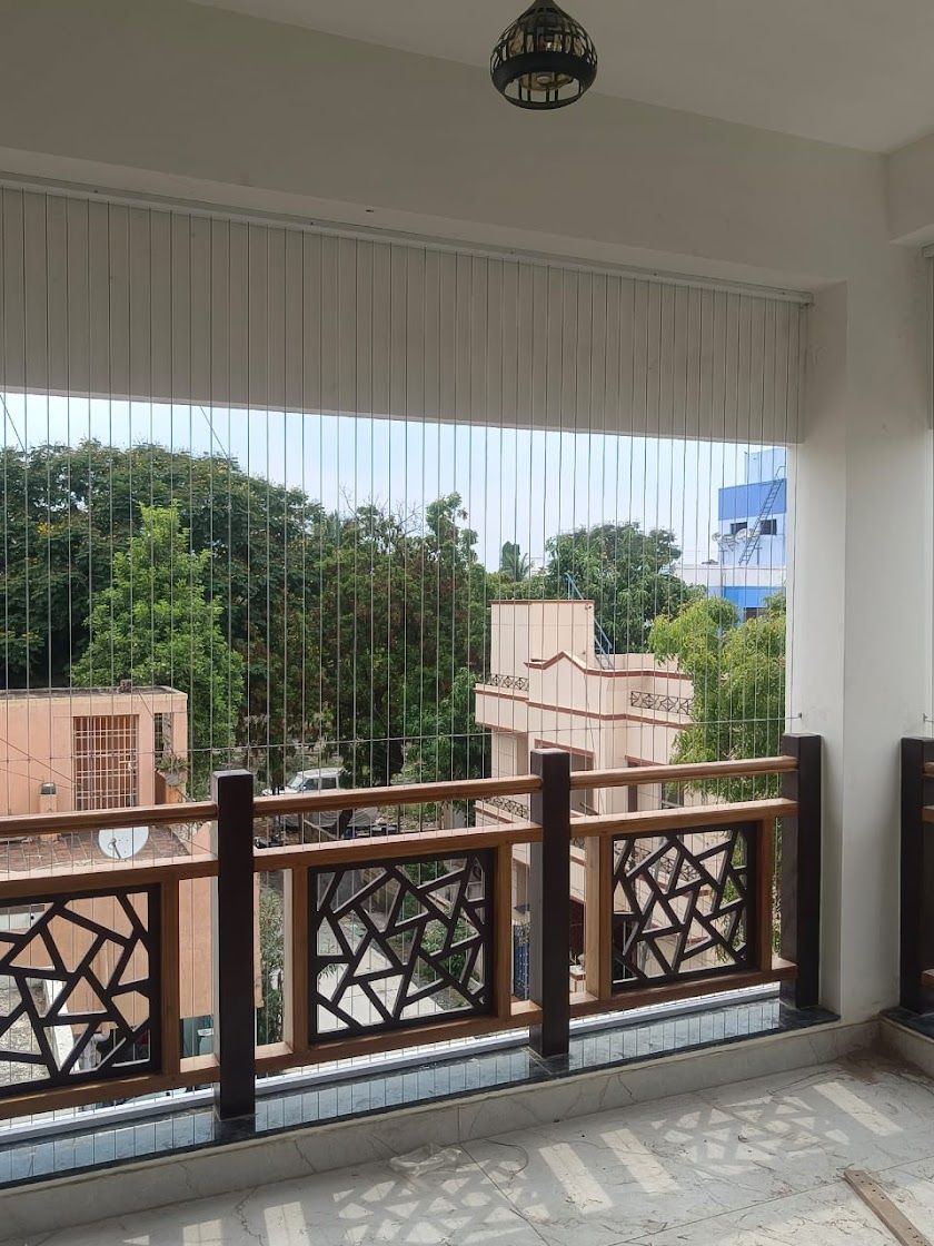 Covered balcony with vertical invisible grills, decorative wooden railing, and views of trees and neighboring homes.